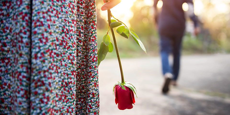 girl holding a rose by her side as man walks away
