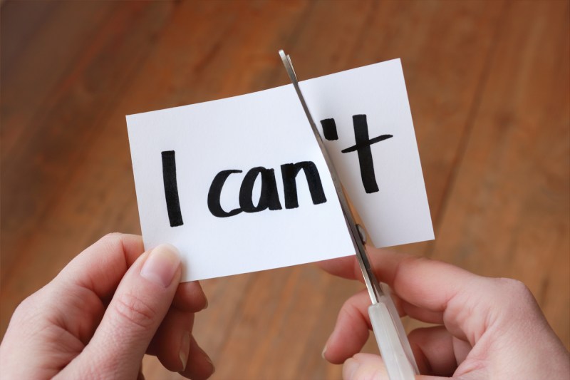 Hands cutting up a small piece of paper that says "I can't" to turn it into "I can"